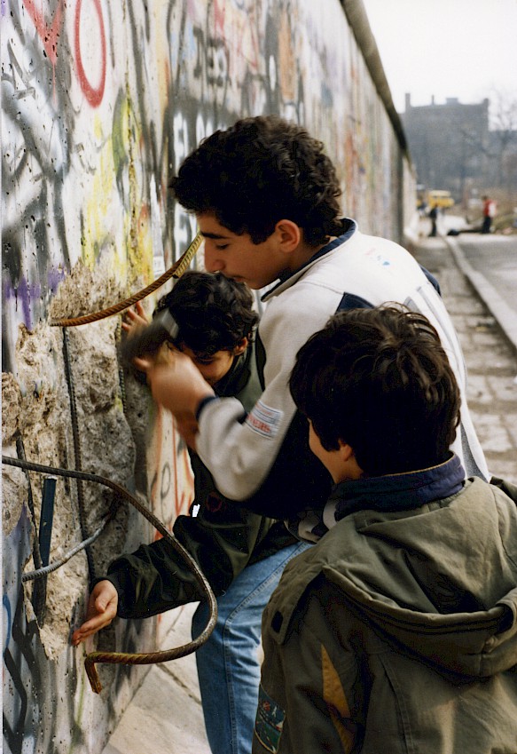 Kinder und Jugendliche aus Kreuzberg schlagen Stücke aus der Mauer heraus. Anschließend verkaufen sie die Mauer-Stücke als Andenken.