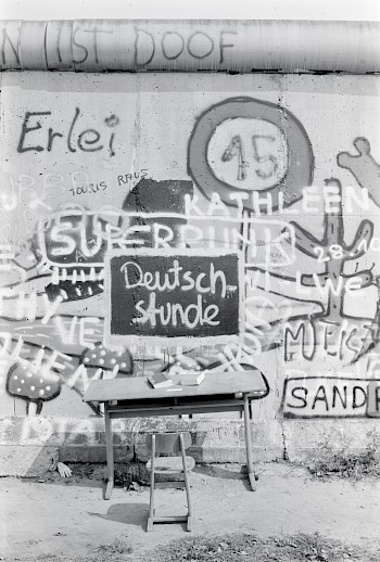 Mauerkünstlerinnen und Mauerkünstler spielten auch mit der Mauer als Objekt, wie hier durch die Ergänzung eines Schultischs und Stuhls an der Mauer am Potsdamer Platz 1986