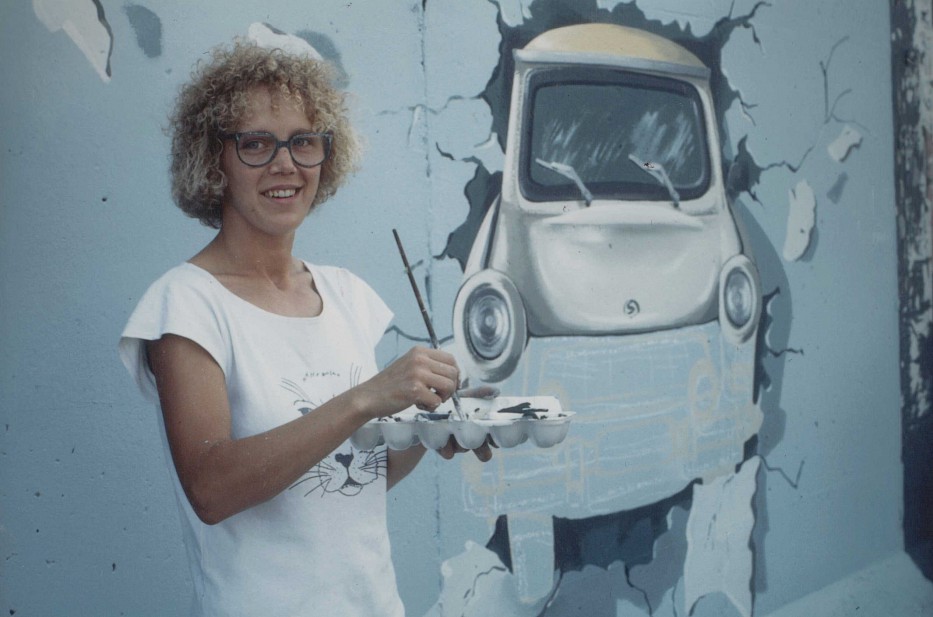 Die Künstlerin Birgit Kinder malt 1990 an der East Side Gallery. Auf ihrem Bild fährt ein Trabi durch die Mauer.